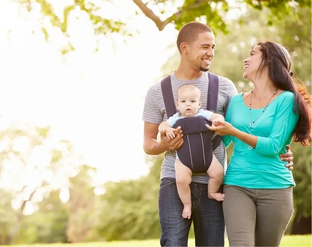 Madre y padre paseando por el parque con su bebé en un portabebé