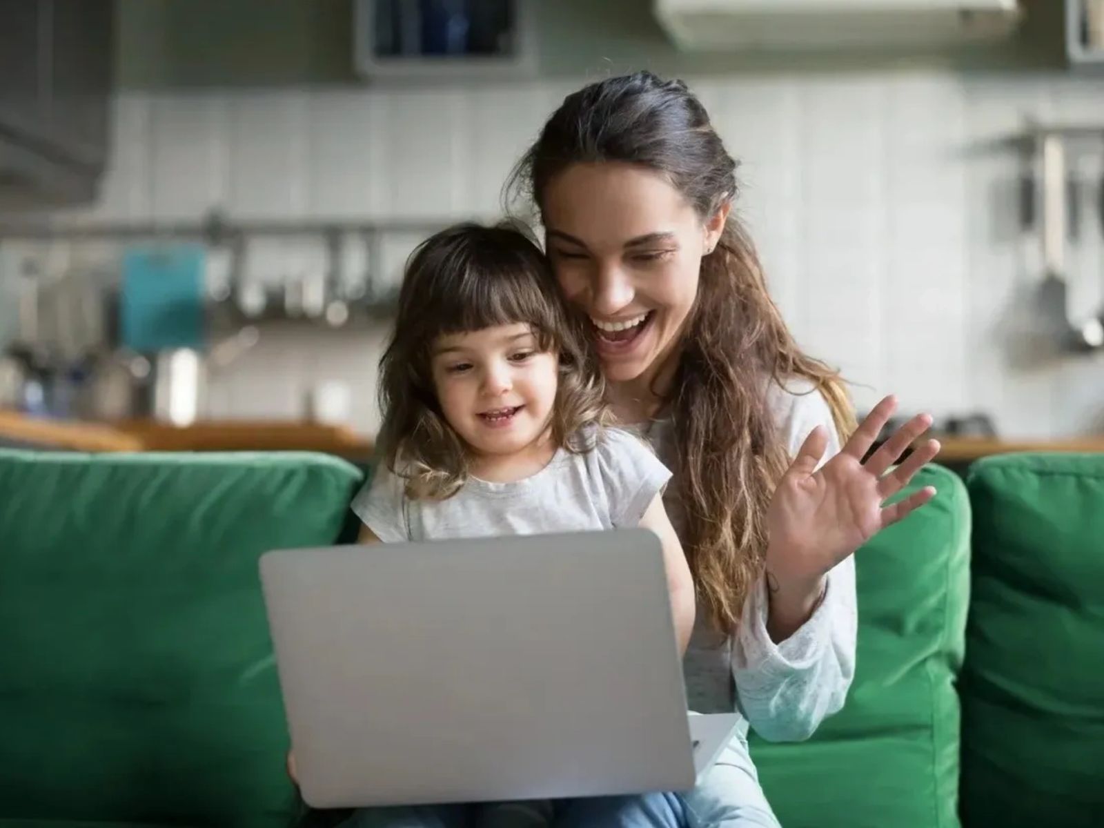 Madre e hija saludan sonrientes durante una videollamada en su computadora